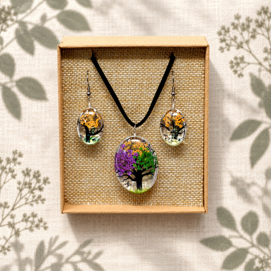 Pressed flower tree-of-life necklace and earrings in a woven box on cream linen with botanical shadows