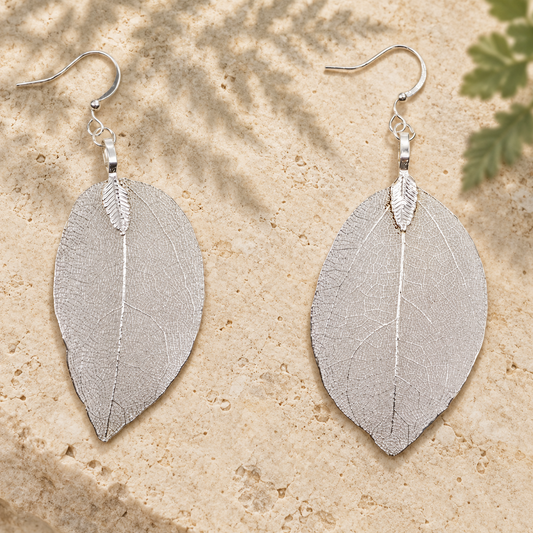 Silver leaf drop earrings on pale stone with a soft botanical shadow